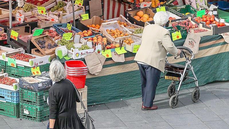 Eine Seniorin steht, gestützt auf ihren Rollator, vor einem Obst- und Gemüsestand auf einem Wochenmarkt. Foto: Jan Woitas/dpa-Zentralbild/dpa