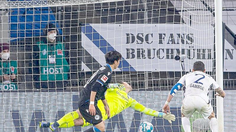 Bielefelds Masaya Okugawa (l) erzielt gegen Bochums Cristian Gamboa (r) und Torwart Manuel Riemann (M) das Führungstor. Foto: Guido Kirchner/dpa