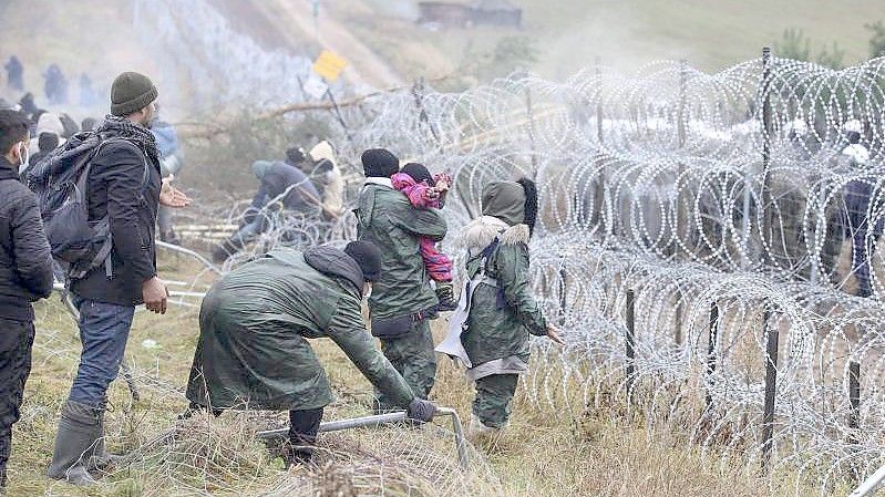 Migranten Anfang November an der belarussisch-polnischen Grenze. Hinter dem Stacheldrahtzaun steht die Polizei. Foto: Leonid Shcheglov/BelTA/AP/dpa