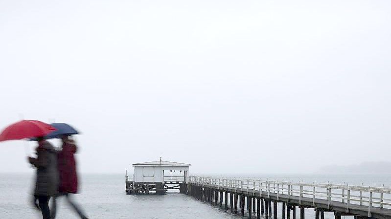 Zwei Personen gehen bei Nieselregen an der Kieler Förde spazieren. Foto: Christian Charisius/dpa