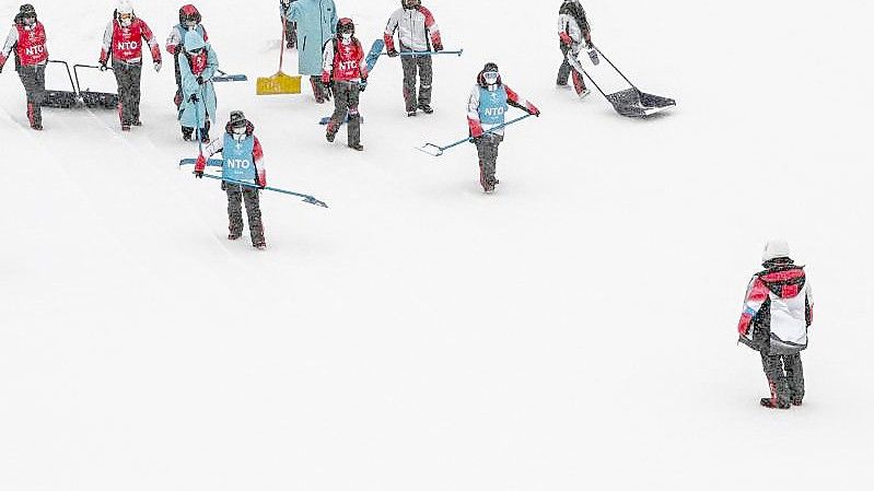 Helfer versuchen die Slopestyle-Piste vom Schnee zu befreien. Foto: Angelika Warmuth/dpa