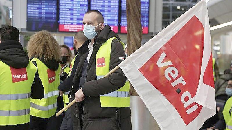 Ein Streikender hält auf einem Flughafen eine Verdi-Flagge. Foto: David Young/dpa