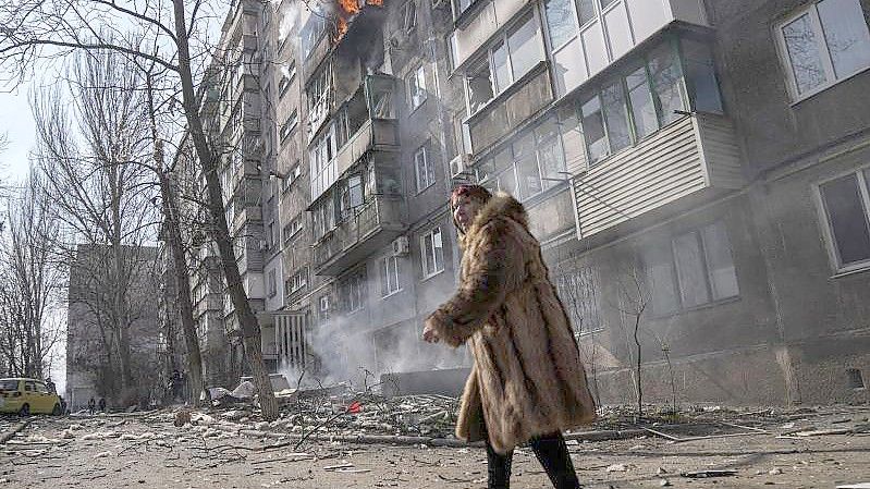 Eine Frau geht an einem brennenden Wohnhaus vorbei, nachdem es beschossen wurde. Foto: Evgeniy Maloletka/AP/dpa
