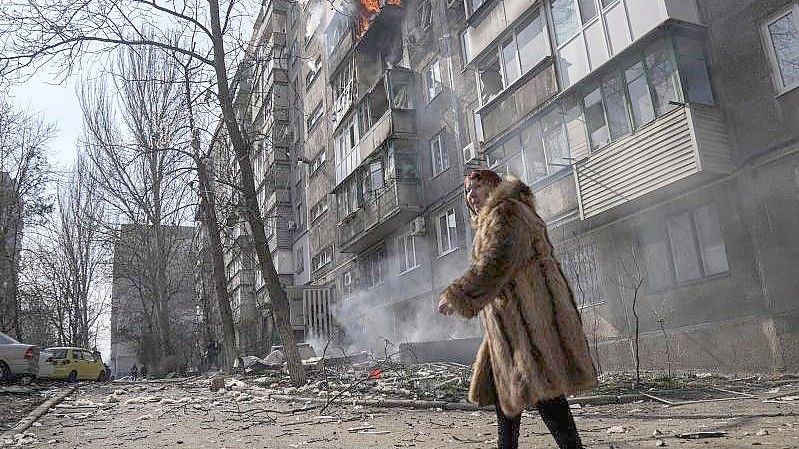 Eine Frau in Mariupol geht an einem brennenden Wohnhaus vorbei. Foto: Evgeniy Maloletka/AP/dpa