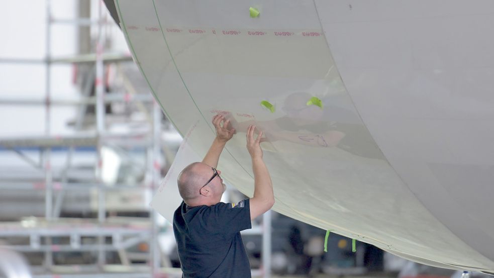 Ein Mitarbeiter bringt bei Lufthansa Technik in Hamburg energiesparende Folie auf einem Flugzeugrumpf an. Foto: Lufthansa Technik