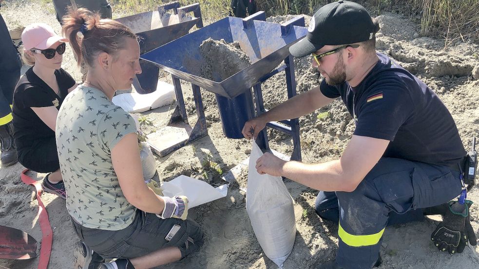 Ein THW-Helfer erläutert Dagmar Pommer (2. von links) und einer weiteren Helferin, wie die Sandsäcke richtig verschlossen werden. Foto: H. Müller