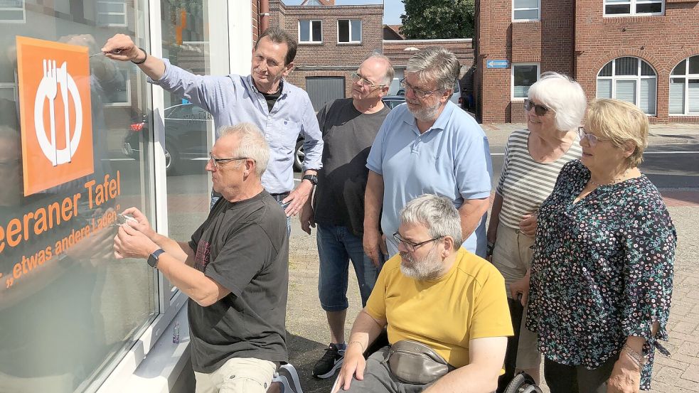 Im Juni taten die Helfer der Leeraner Tafel so, als ob sie das Logo der Tafel von der Scheibe ihres jetzigen Domizils abkratzen. Bald werden Hanna Weidner (von rechts), Heidi Lünemann, Andreas Poppen (vorne), Andreas Bartels, Wolfgang Mallik, Johannes Pauw (hinten) und Detlev Hartmann tatsächlich Hand anlegen – vermutlich spätestens im Sommer. Foto: Mielcarek/Archiv