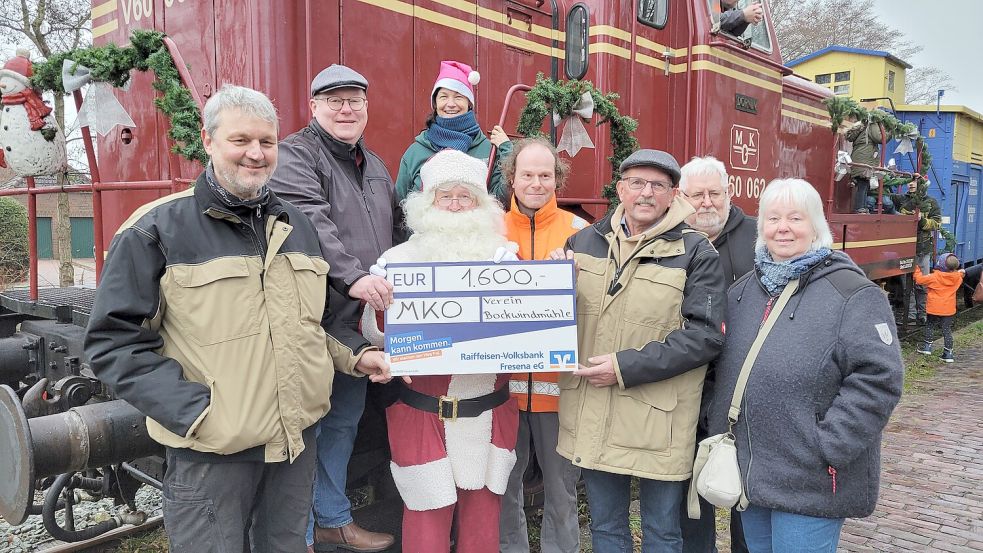 Mühlenwart Fred Hoppen (von links), MKO-Vorsitzender Christian Walther, stellvertretende MKO-Vorsitzende Bettina Schüttler, Nikolaus und stellvertretender MKO-Vorsitzender Andreas van Dieken, MKO-Schatzmeister Henning Immoor, Mühlenverein Vorsitzender Wilhelm Broeksmid, Mühlensekretär Michael Röthling und Mühlenkassenwartin Gabi Henning bei der Scheckübergabe am Bahnhof Dornum. Foto: Rebecca Kresse