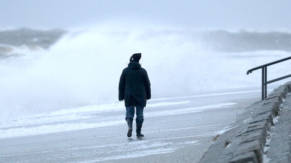 Eine Spaziergängerin läuft bei stürmischem Wetter am Nordstrand der ostfriesischen Insel Norderney. Foto: Bartels/dpa