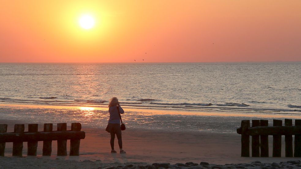 Eine Frau fotografiert am Strand der Insel Wangerooge einen Sonnenuntergang über der Nordsee. Foto: Kuchenbuch-Hanken/DPA