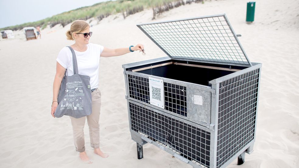 Nadine Weber, Projektkoordinatorin für Nachhaltigkeit und Klimaschutz auf Spiekeroog, steht mit einer sogenannten Strandmülltasche an einer Strandmüllbox auf der Insel. Auf Spiekeroog soll die grüne und nachhaltige Ausrichtung weiter verstärkt werden, langfristig soll die Insel klimaneutral werden. Foto: Hauke-Christian Dittrich/dpa