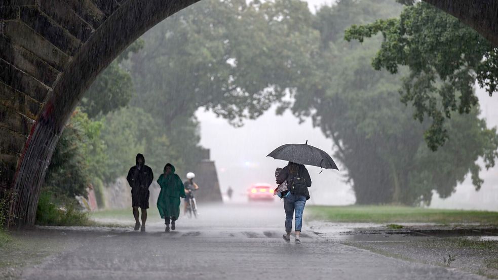 Menschen sind bei starkem Regen in Dresden während eines Gewitters auf dem Elberadweg unterwegs. Foto: Robert Michael/dpa