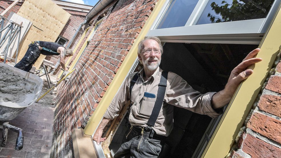 Holger Rodiek zeigt die neuen Fenster. Im Hintergrund setzen Handwerker die Tür ein. Der Rahmen wurde sandsteinfarben, die Fenster in einem Grauton gestrichen. Foto: Ortgies