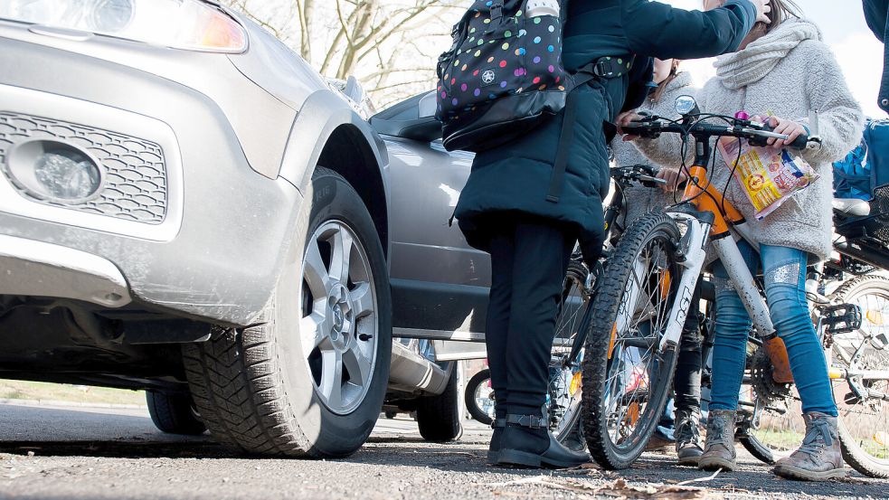 Schülerinnen mit ihren Fahrrädern stehen auf einem Gehweg, auf dem ein Elterntaxi steht. Symbolfoto: Pförtner/dpa