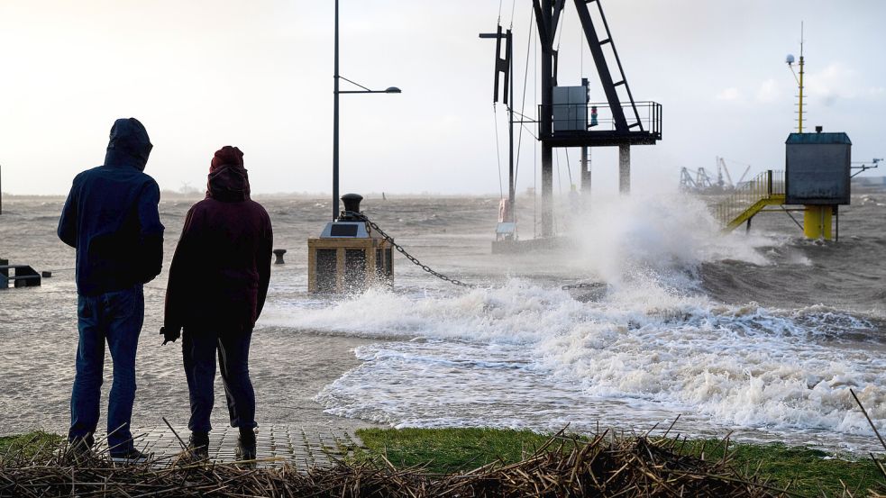 Spaziergänger laufen bei Sturmflut am Ufer der Wesermündung in Bremerhaven. Das Bild entstand im Dezember 2023. Foto: Schuldt/dpa