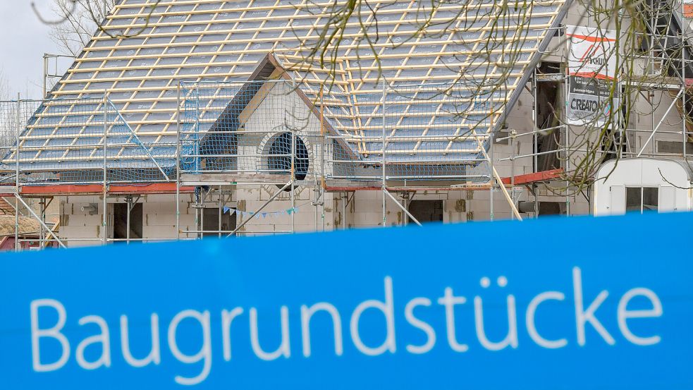 Ein Schild mit der Aufschrift „Baugrundstücke“ steht am Rande eines Baufeldes, auf dem ein Eigenheim entsteht. Finanzierungs-, Bau- und Grundstückskosten sind in Ostfriesland gestiegen. Foto: Patrick Pleul/ZB/dpa