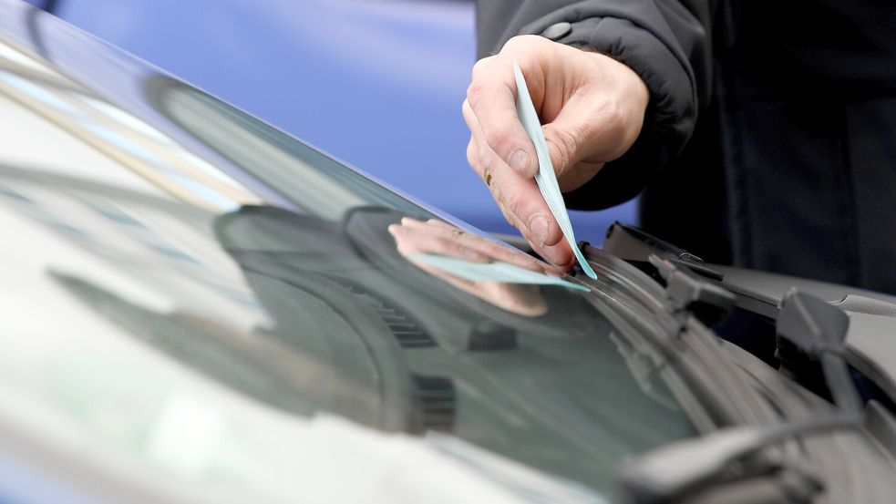 Jemand klemmt einen Strafzettel hinter den Scheibenwischer eines Autos. Symbolfoto: Dedert/dpa