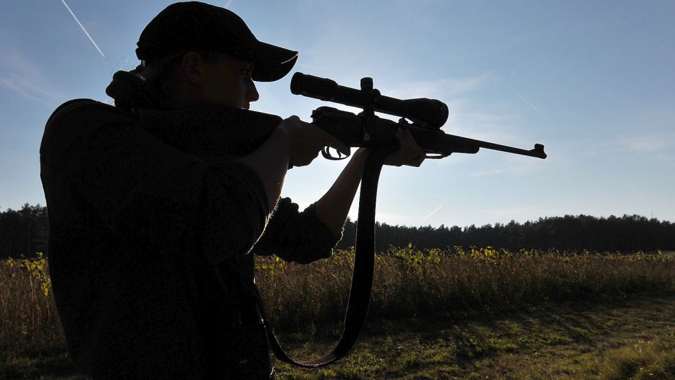 Eine Jägerin steht mit ihrem Gewehr in einem Waldstück. Foto: Philipp Schulze/dpa