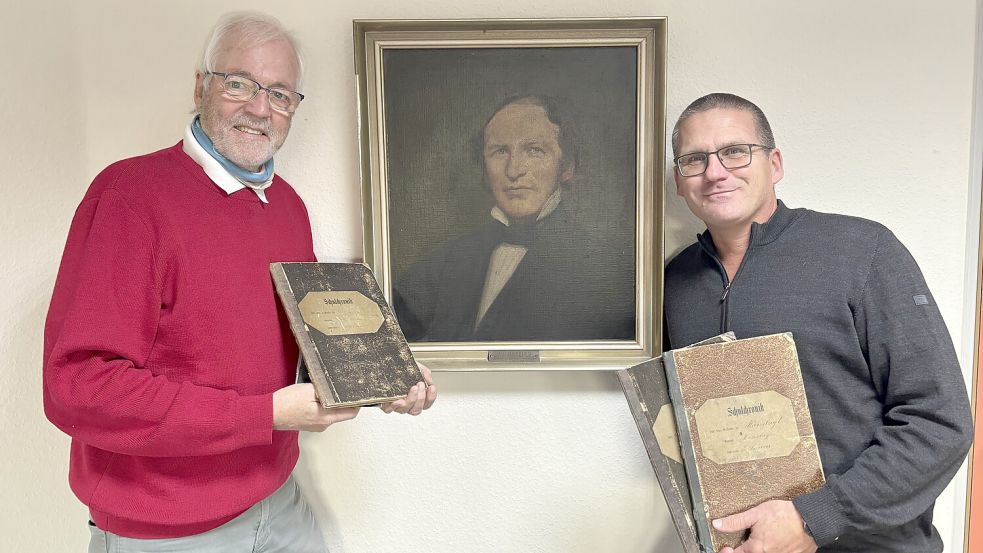 Hobbyhistoriker Helmut Fischer (links) und Schulleiter Hauke Piper mit den alten Schulchroniken aus Greetsiel, Manslagt und Pilsum. In der Mitte ist ein Gemälde von Lehrer A. Hobbing zu sehen. Foto: Weiden