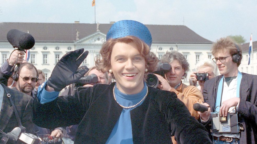 Verkleidet als Königin Beatrix winkt der deutsche Komiker und Showmaster Hape Kerkeling vor Schloss Bellevue für die Presse. (Archivfoto von 1991) Foto: picture alliance / dpa