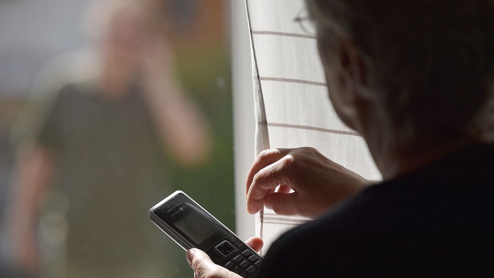 Eine Frau steht mit einem Telefon am Fenster, vor dem ein Mann steht (gestellte Szene). Foto: Warmuth/dpa