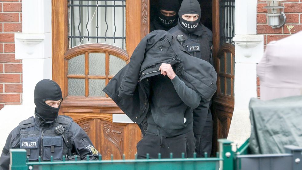 Polizeibeamte führen einen Tatverdächtigen aus einem durchsuchten Haus. Foto: Christoph Reichwein/dpa